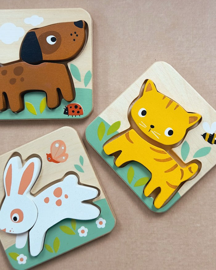 Three wooden animal puzzles of a dog, cat, and rabbit on a beige background.