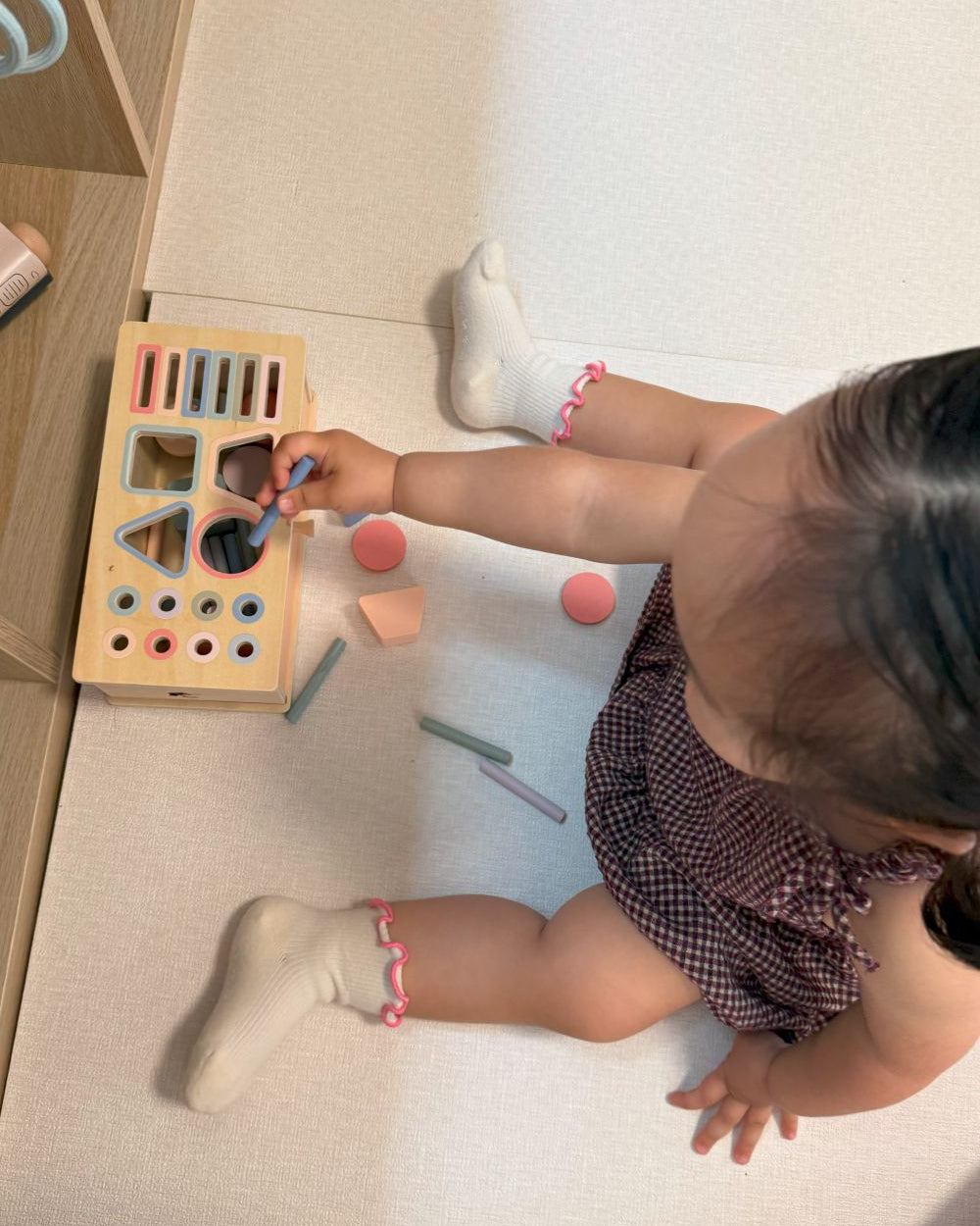 Child playing with a shape sorting toy on a light-colored floor.