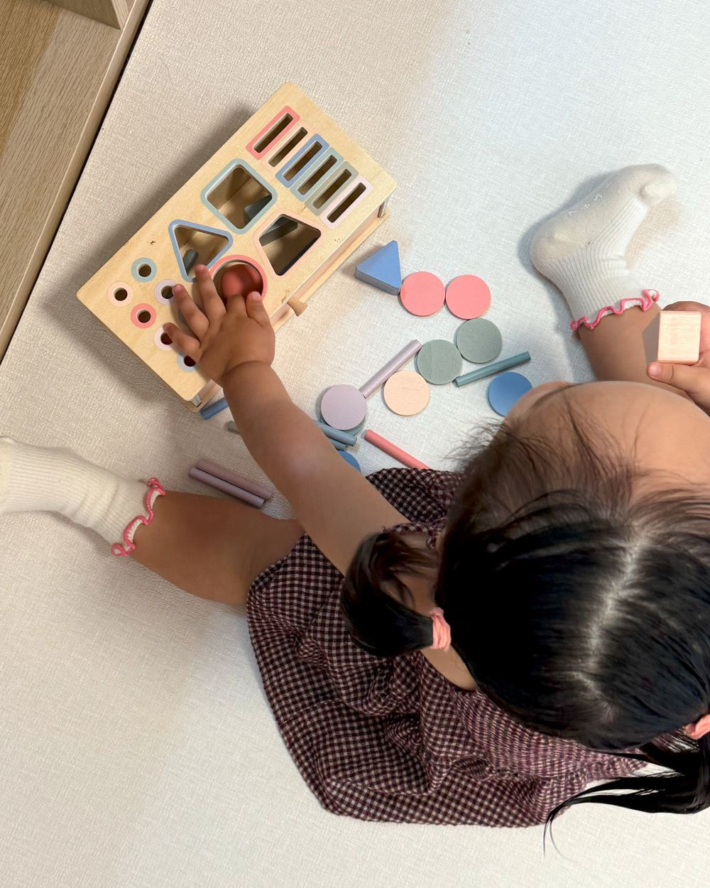 Child playing with a shape sorting toy on a light-colored floor.