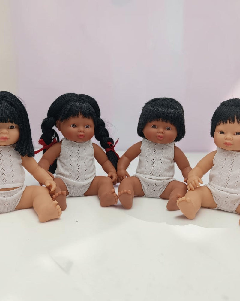 Four dolls with black hair and white outfits sitting on a light surface.