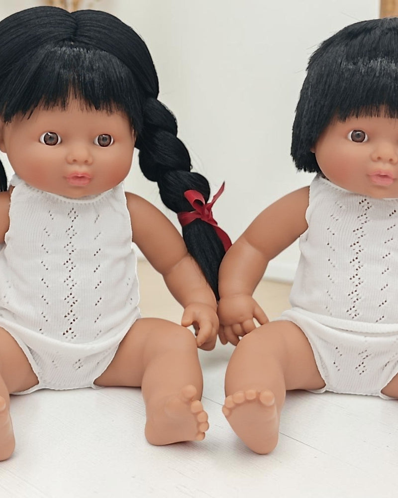 Two dolls with black hair and white outfits sitting on a light surface.