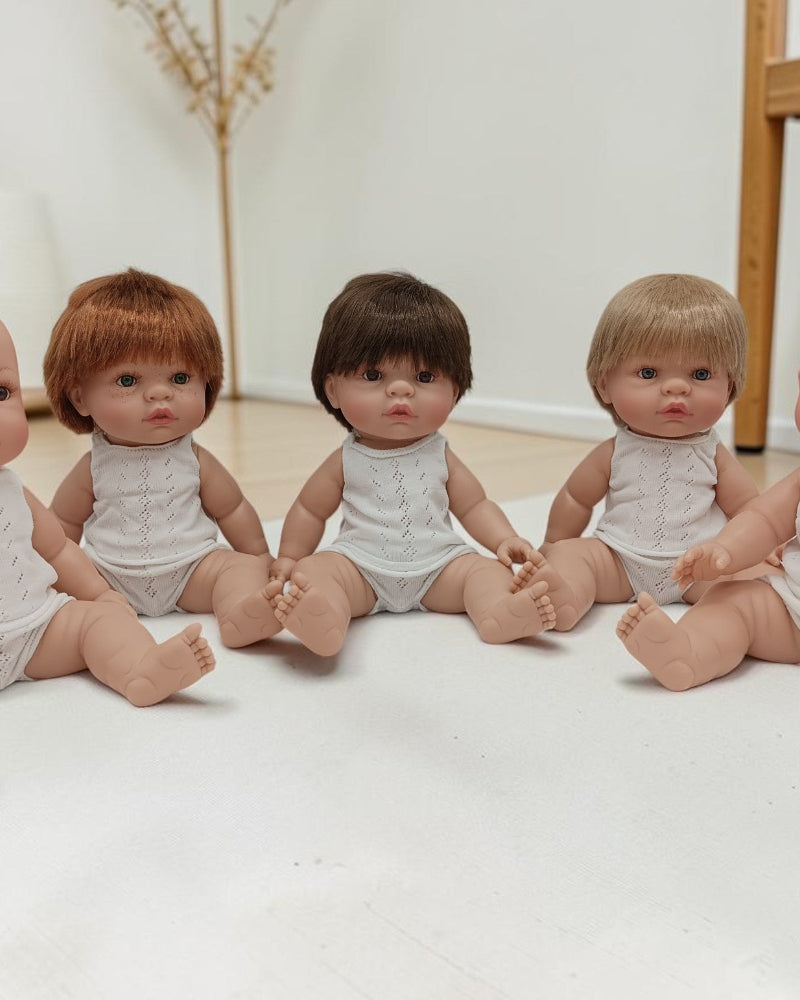 Five baby dolls with different hair colors sitting on a white mat.