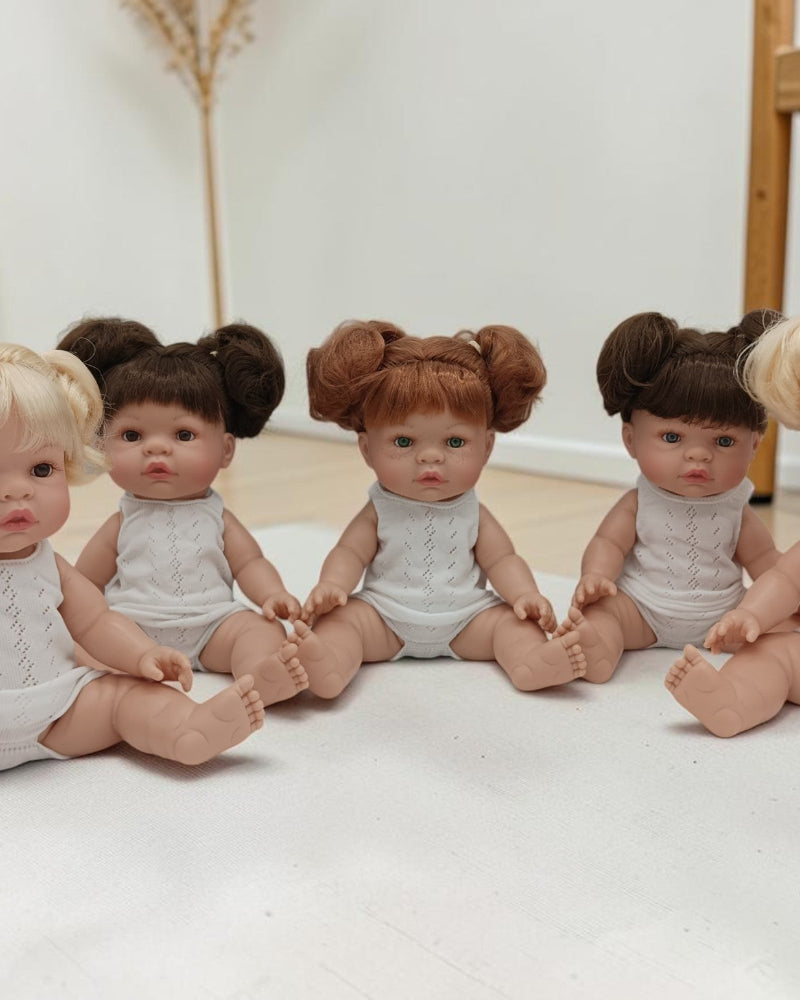 Five dolls with styled hair sitting on a white surface.