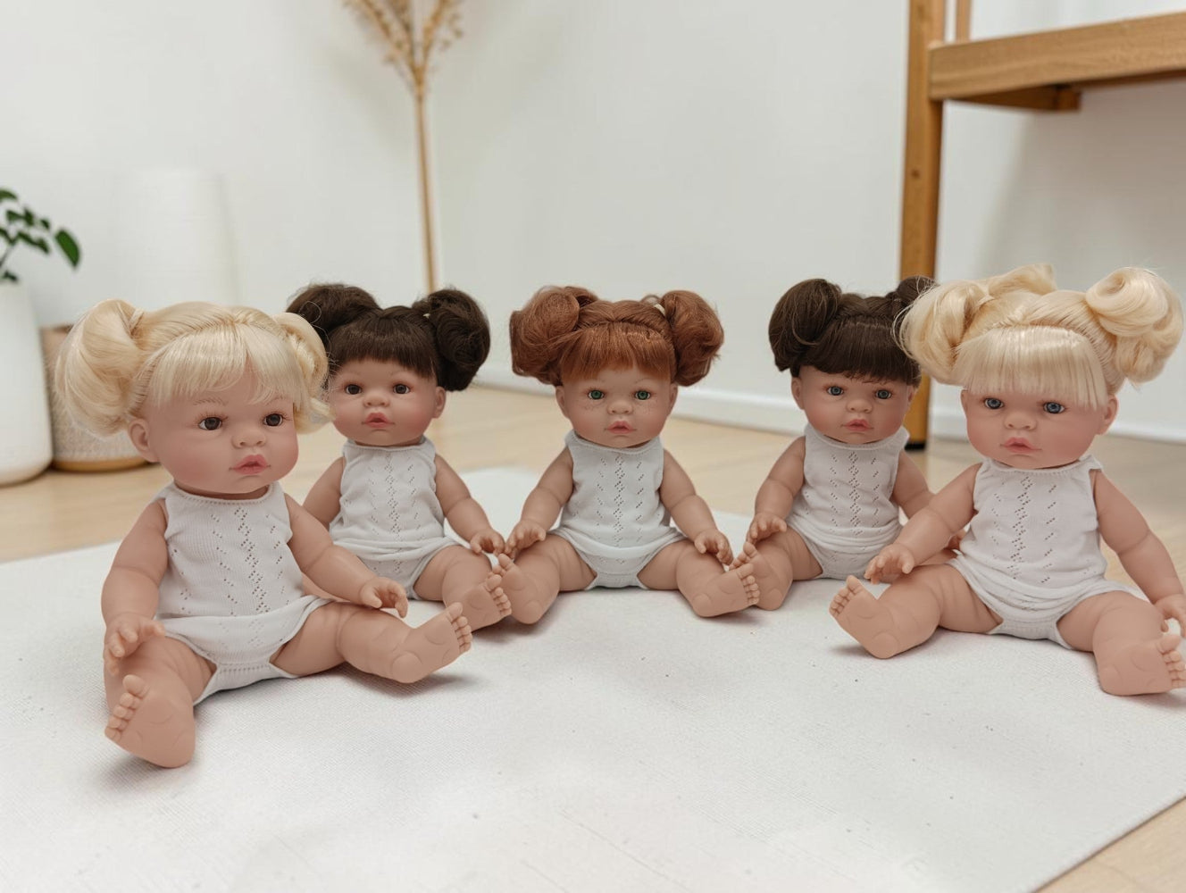 Five dolls with styled hair sitting on a white surface.