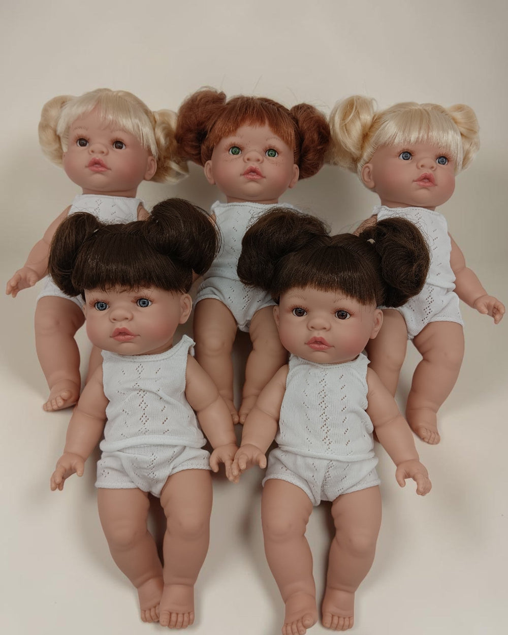 Five dolls with styled hair in pigtails on a plain background