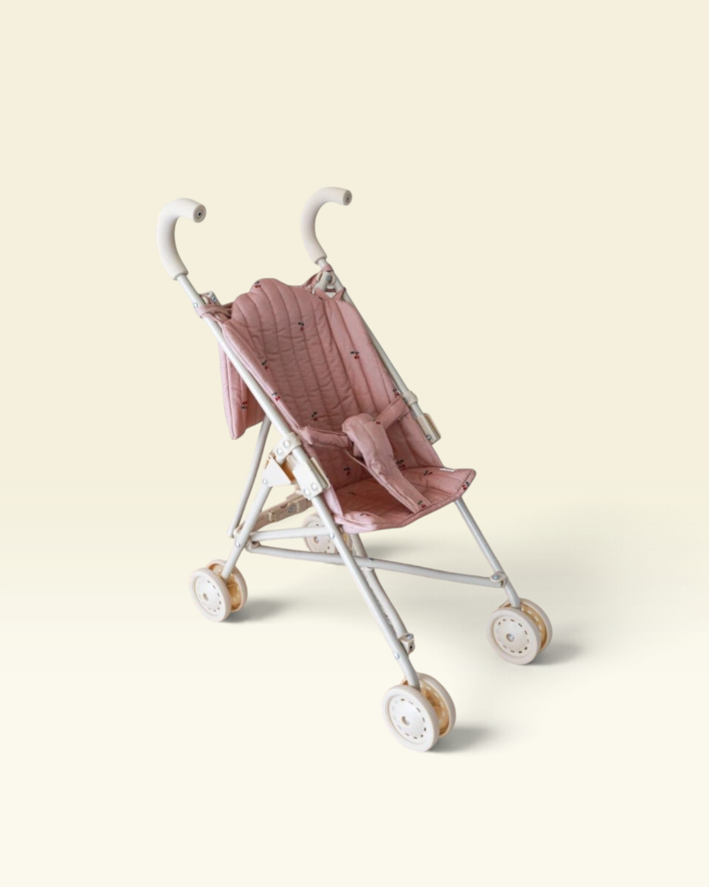 A vintage-style baby stroller with a dusty pink quilted fabric seat and canopy, supported by a silver metal frame with white-washed wheels, set against a solid pale cream background.