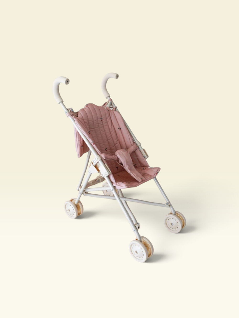 A vintage-style baby stroller with a dusty pink quilted fabric seat and canopy, supported by a silver metal frame with white-washed wheels, set against a solid pale cream background.