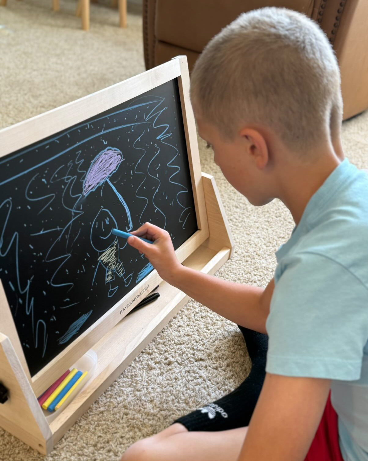 Child drawing on a blackboard with a blue marker indoors.