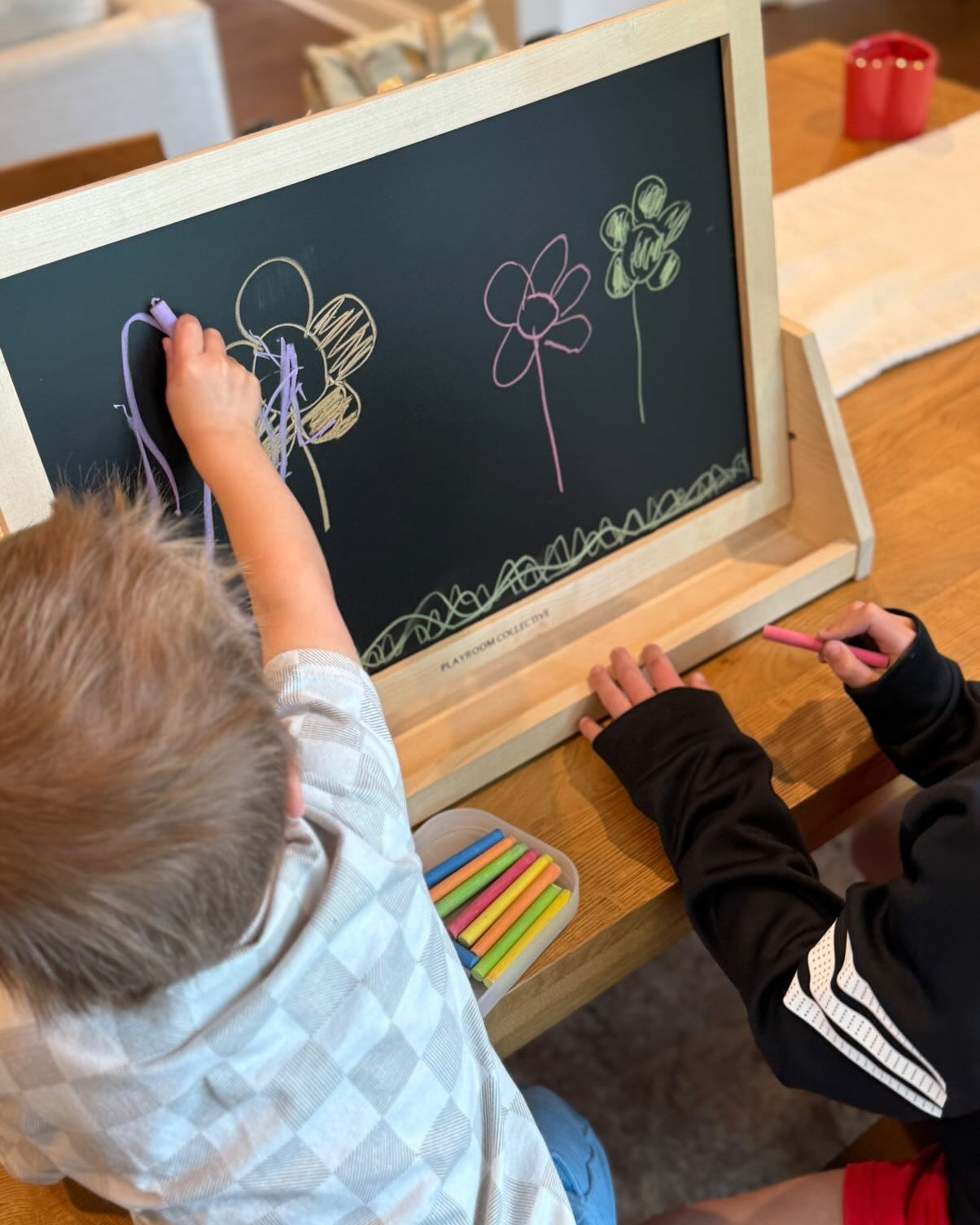 Two children drawing on a small chalkboard with colorful chalks.