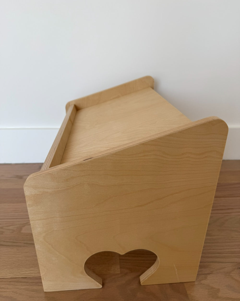 Wooden pet bed with a heart-shaped opening on a wooden floor.