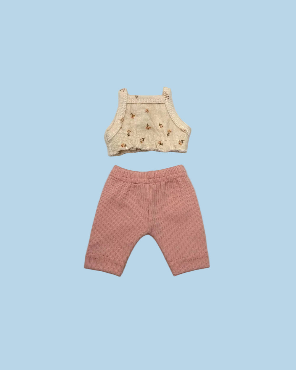 A two-piece baby outfit set laid flat on a light gray background, featuring a cream-colored sleeveless top with a small brown floral pattern and matching pink ribbed shorts.