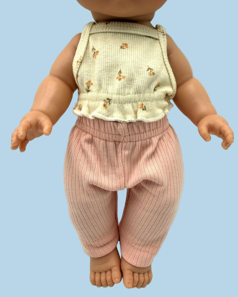 A doll or toy figure wearing a sleeveless cream top with small tan floral motifs and pink ribbed pants, photographed against a plain light background.