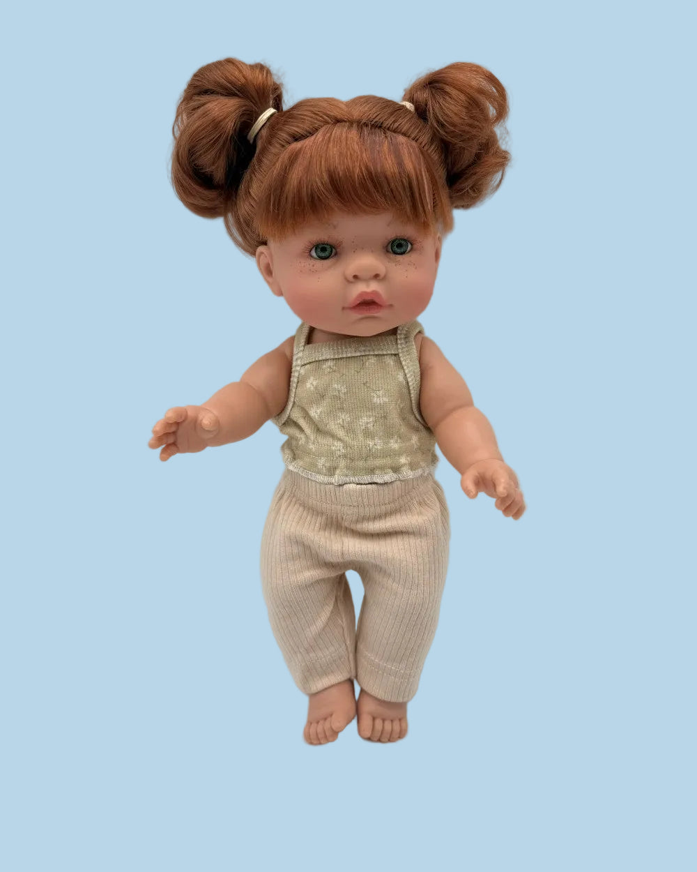 A doll with brown hair in two buns, wearing a beige patterned sleeveless top and matching ribbed pants, photographed against a plain light gray background.
