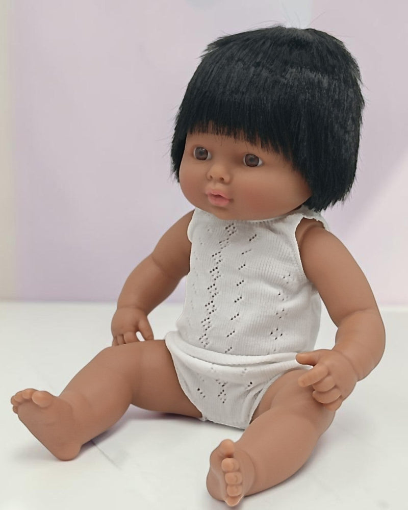 Doll with black hair wearing a white outfit on a light background
