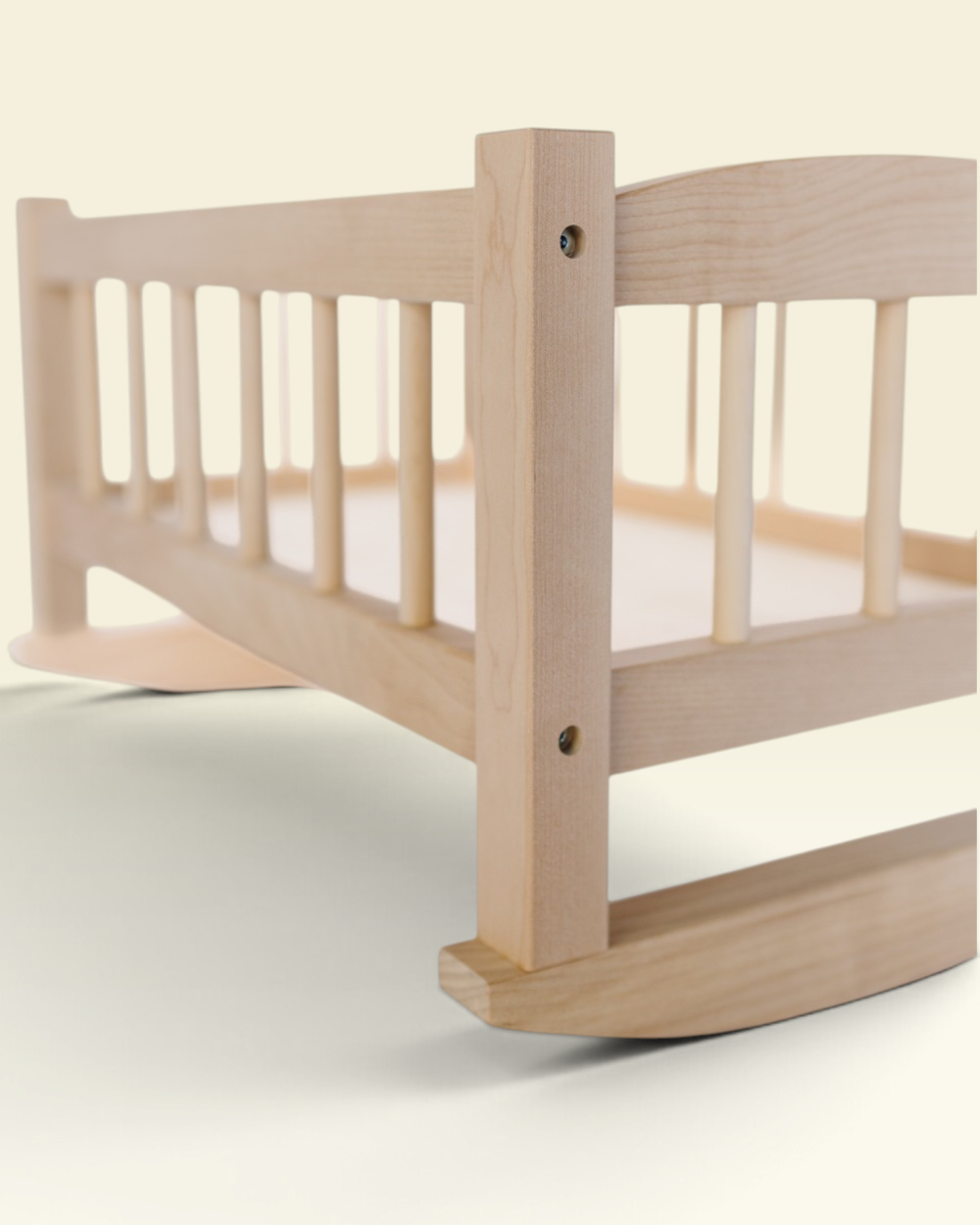 A close-up of a light natural wood rocking bed frame, showing the slatted side rail, corner post, and curved rocker base against a soft cream background.