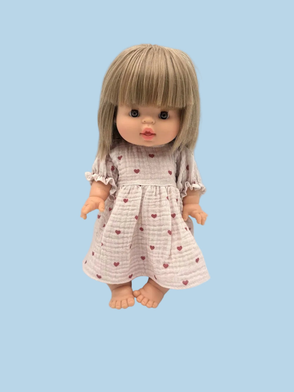 Doll with blonde hair and a pink dress with red hearts on a light blue background