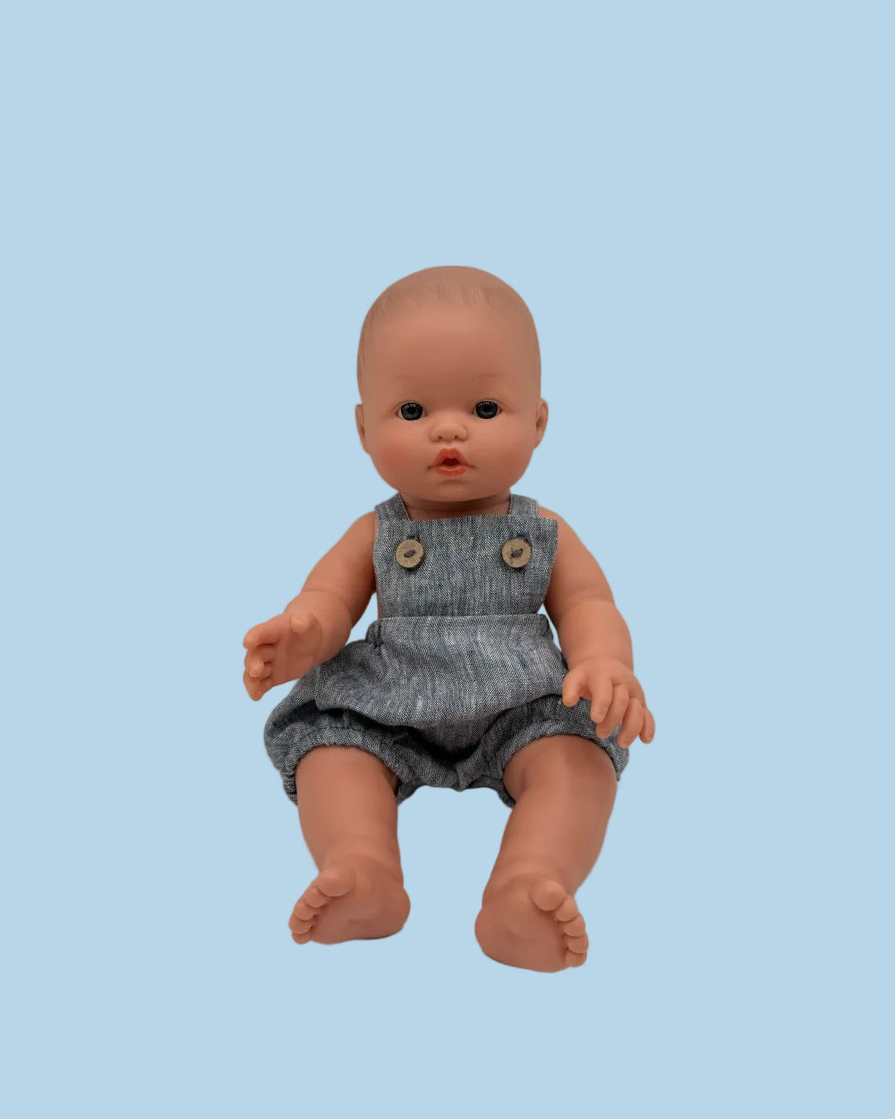 Baby doll wearing a denim romper on a plain background