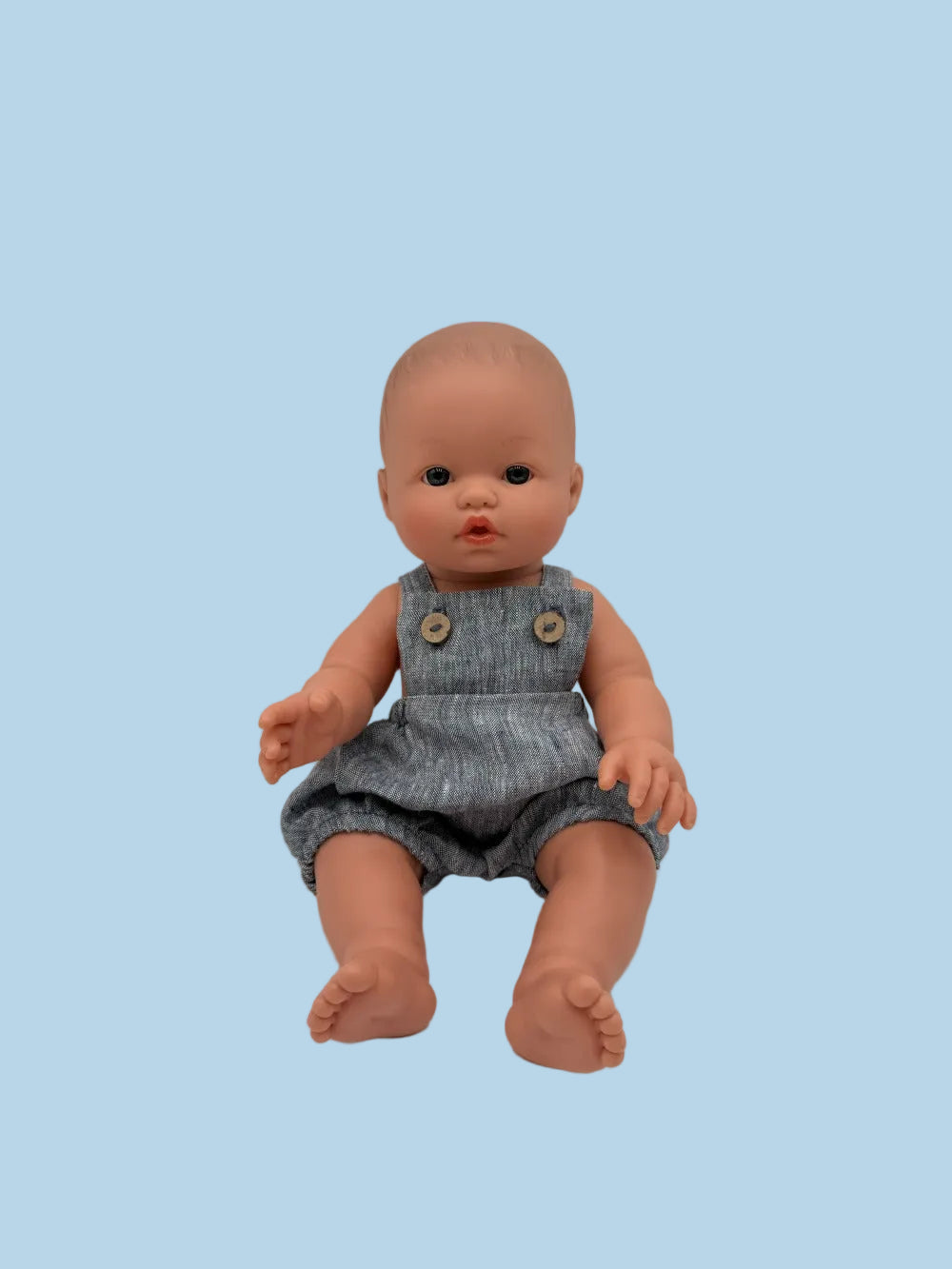 Baby doll wearing a denim romper on a plain background