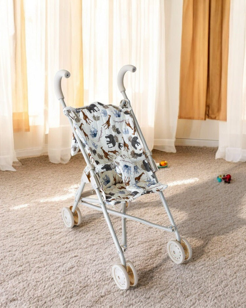 A white baby doll stroller with a pattern featuring elephants and other safari animals in browns and blues, displayed in a room setting.
