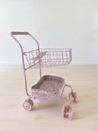 Side view of pink floral doll cart showing two-tier design with upper basket and padded lower seat platform