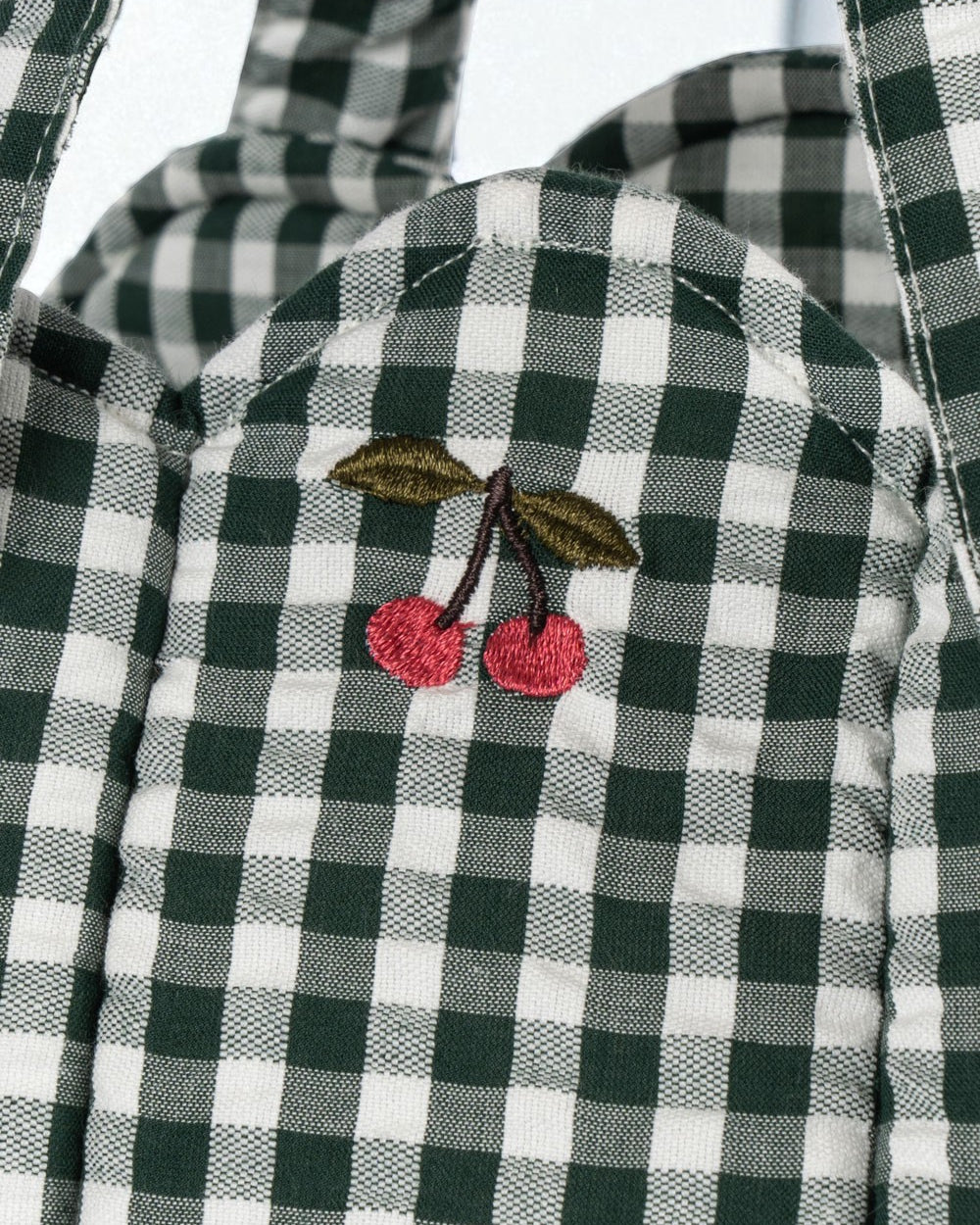 Close-up of embroidered cherry accent on green and white checkered bassinet showing charming decorative detail