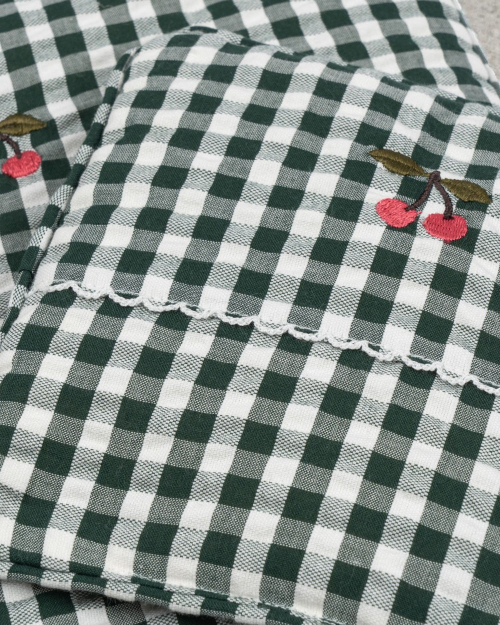 Close-up of embroidered cherry accent on green check bedding showing charming farmhouse decorative detail