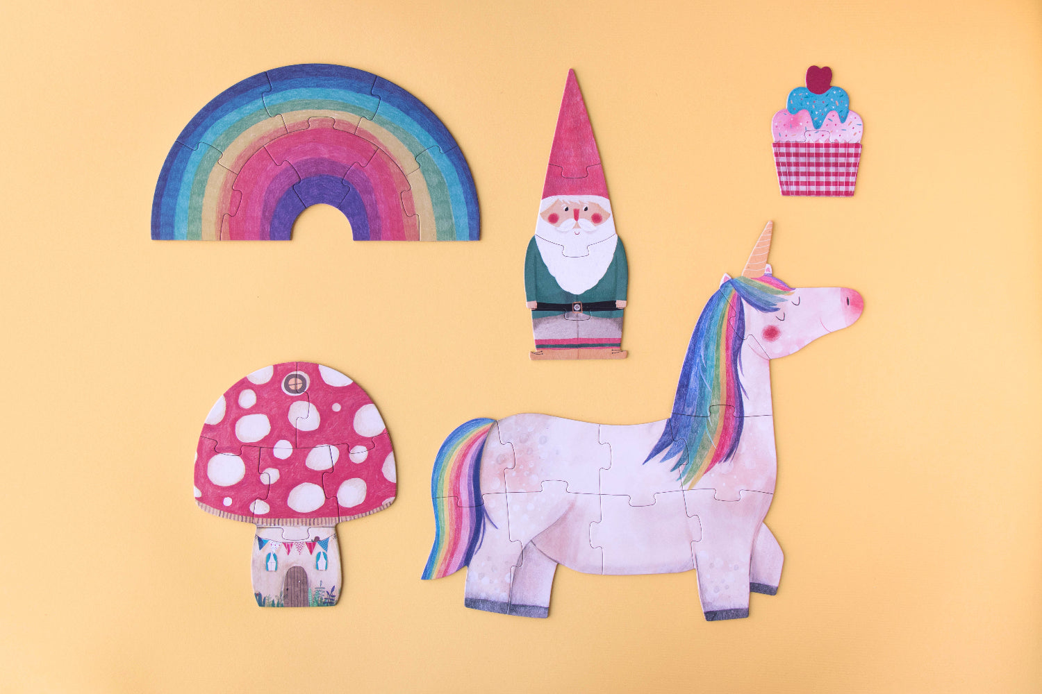 Colorful paper cutouts of a unicorn, mushroom, gnome, rainbow, and cupcake on a yellow background