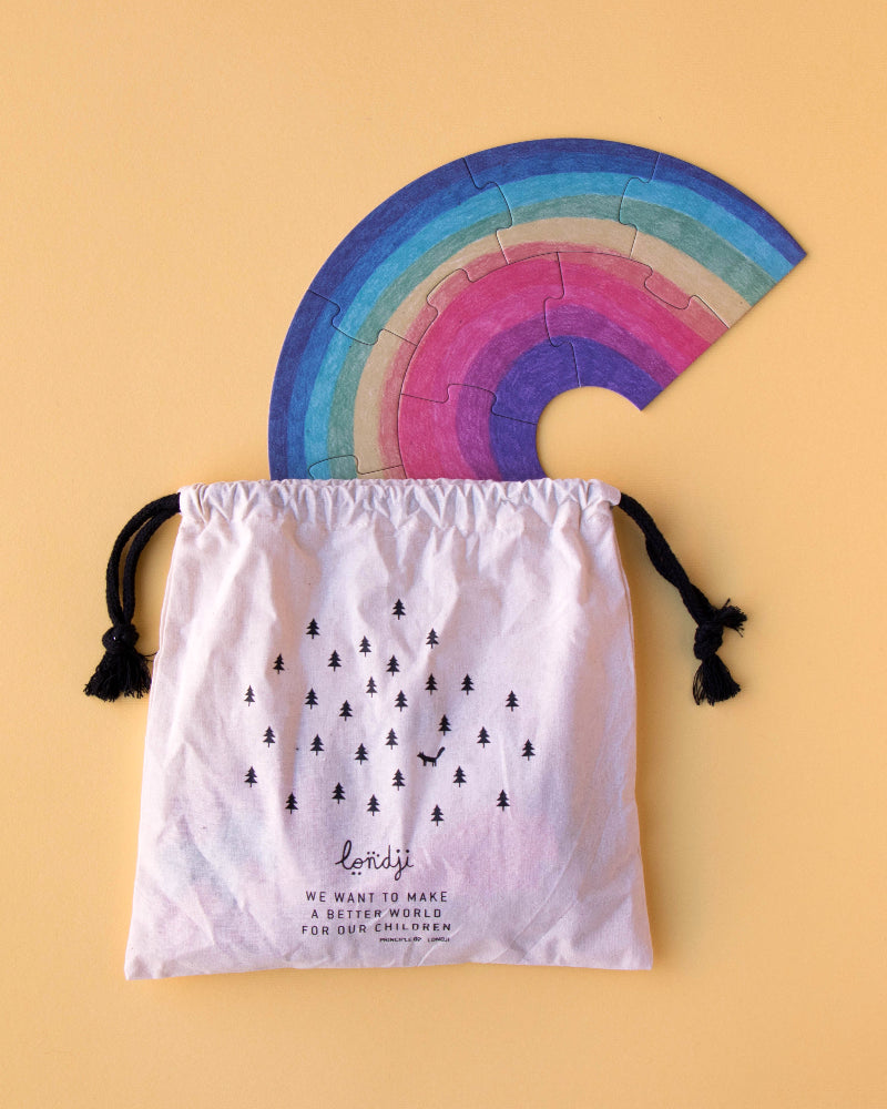 Colorful rainbow-shaped object on a white drawstring bag with text against a beige background