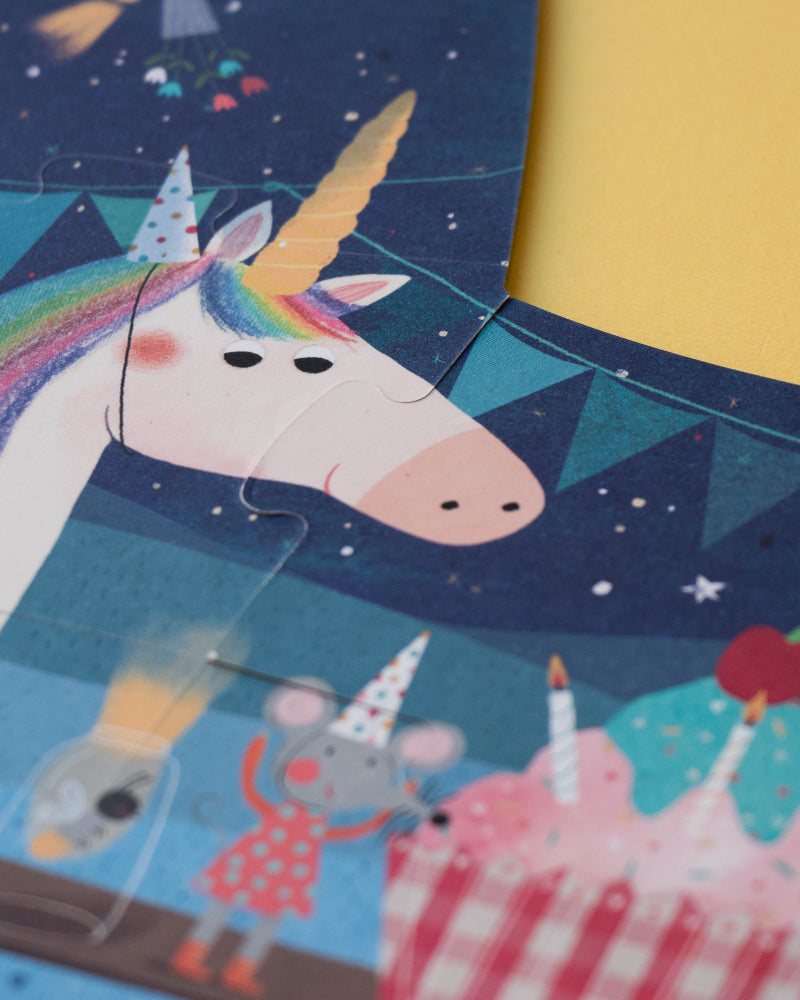 Children's puzzle with a unicorn, cake, and birthday-themed pieces on a blue and yellow background.
