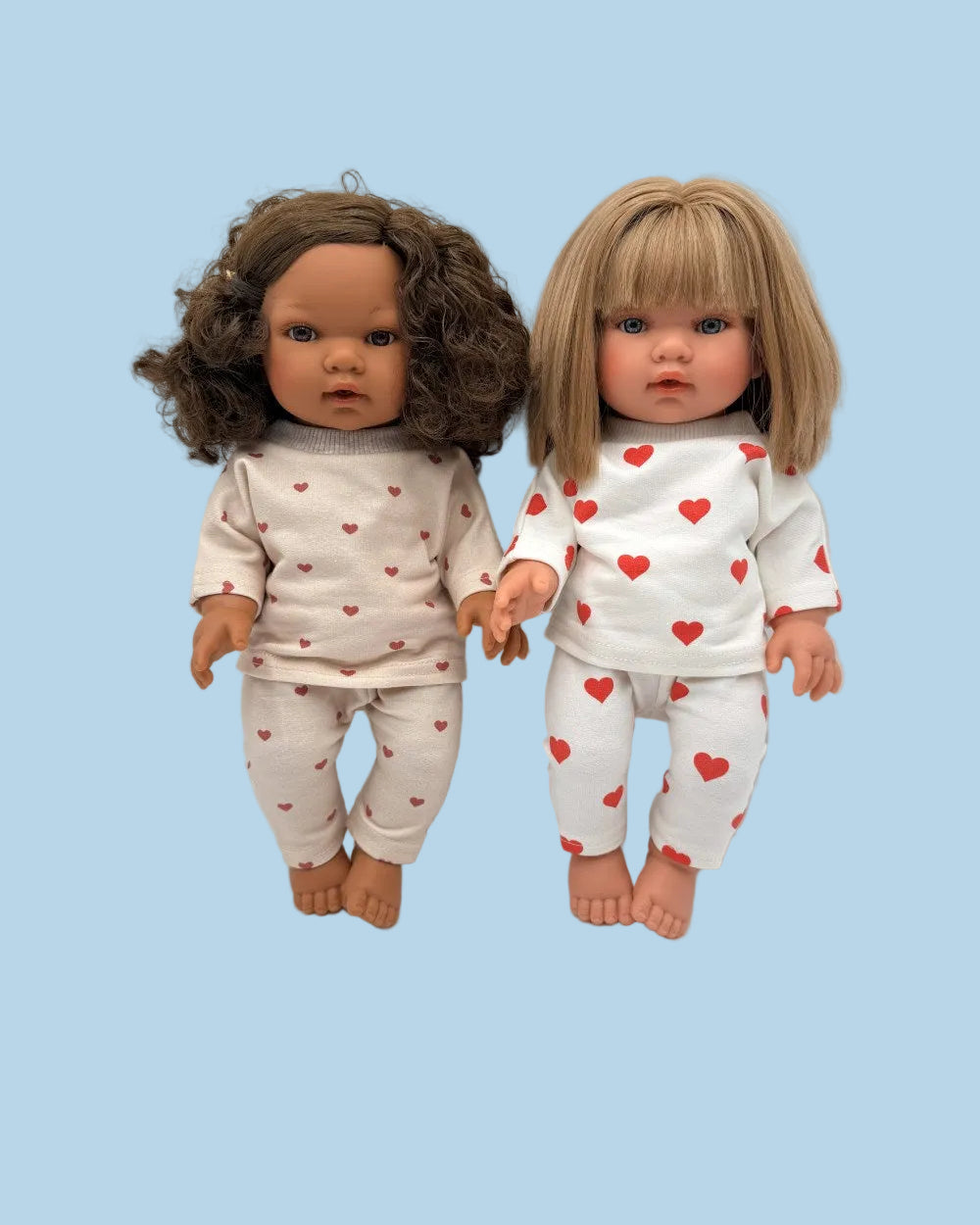Two dolls wearing matching pajamas with red hearts on a white background