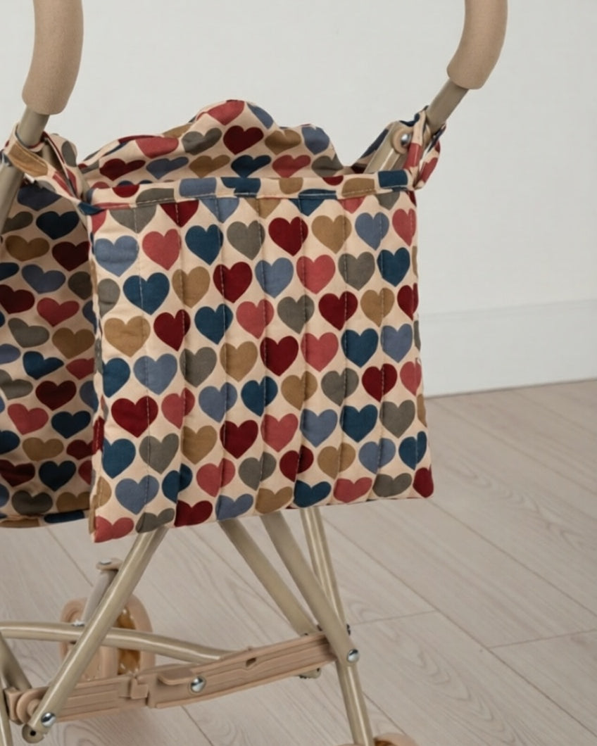 Stroller with a colorful heart-patterned cover on a wooden floor.