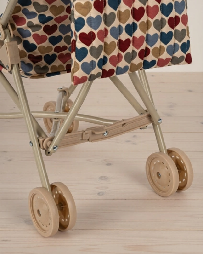 Miniature stroller with a heart-patterned cover on a wooden floor
