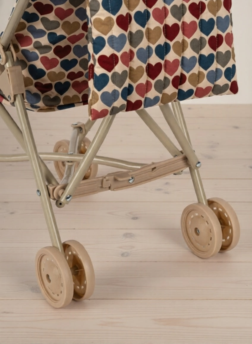 Miniature stroller with a heart-patterned cover on a wooden floor