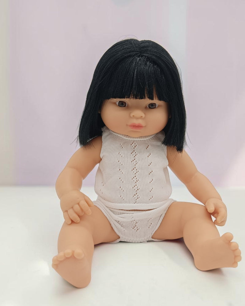 Doll with black hair wearing a white outfit on a light background
