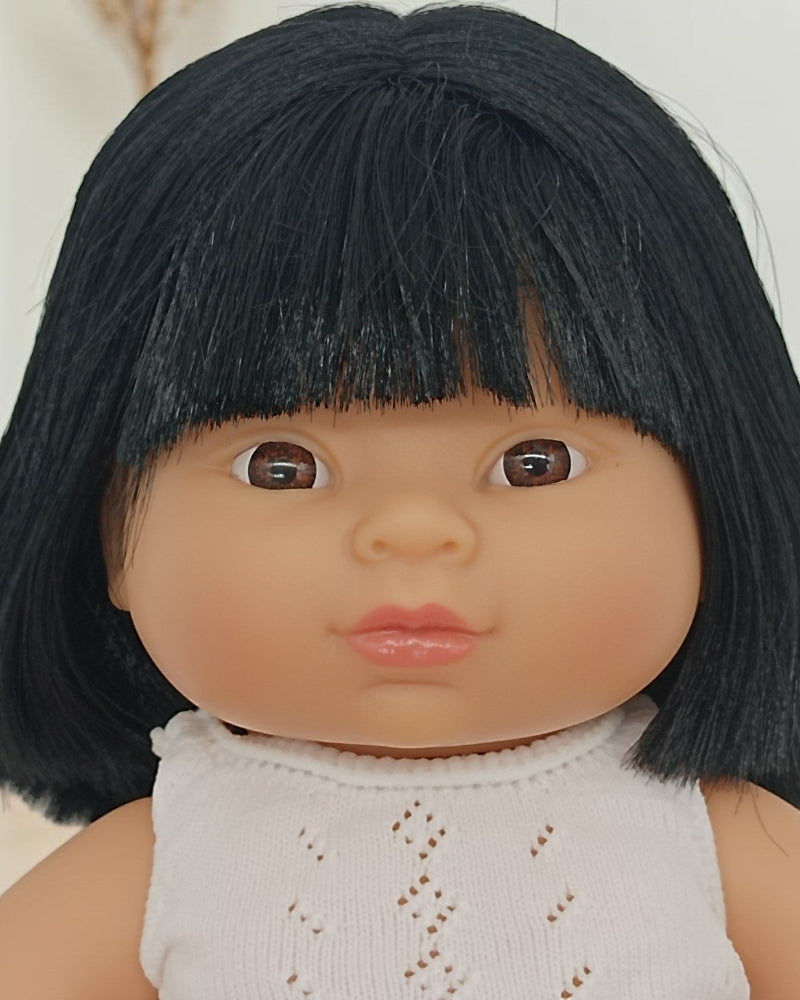 Doll with black hair and a white outfit against a neutral background