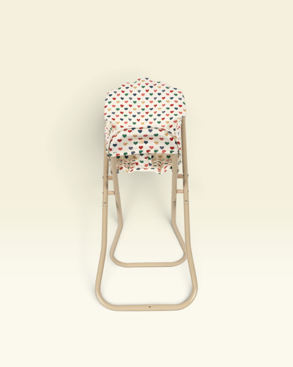 A baby carrier seat insert with a colorful heart pattern, shown on a beige metal high chair against a solid cream background.