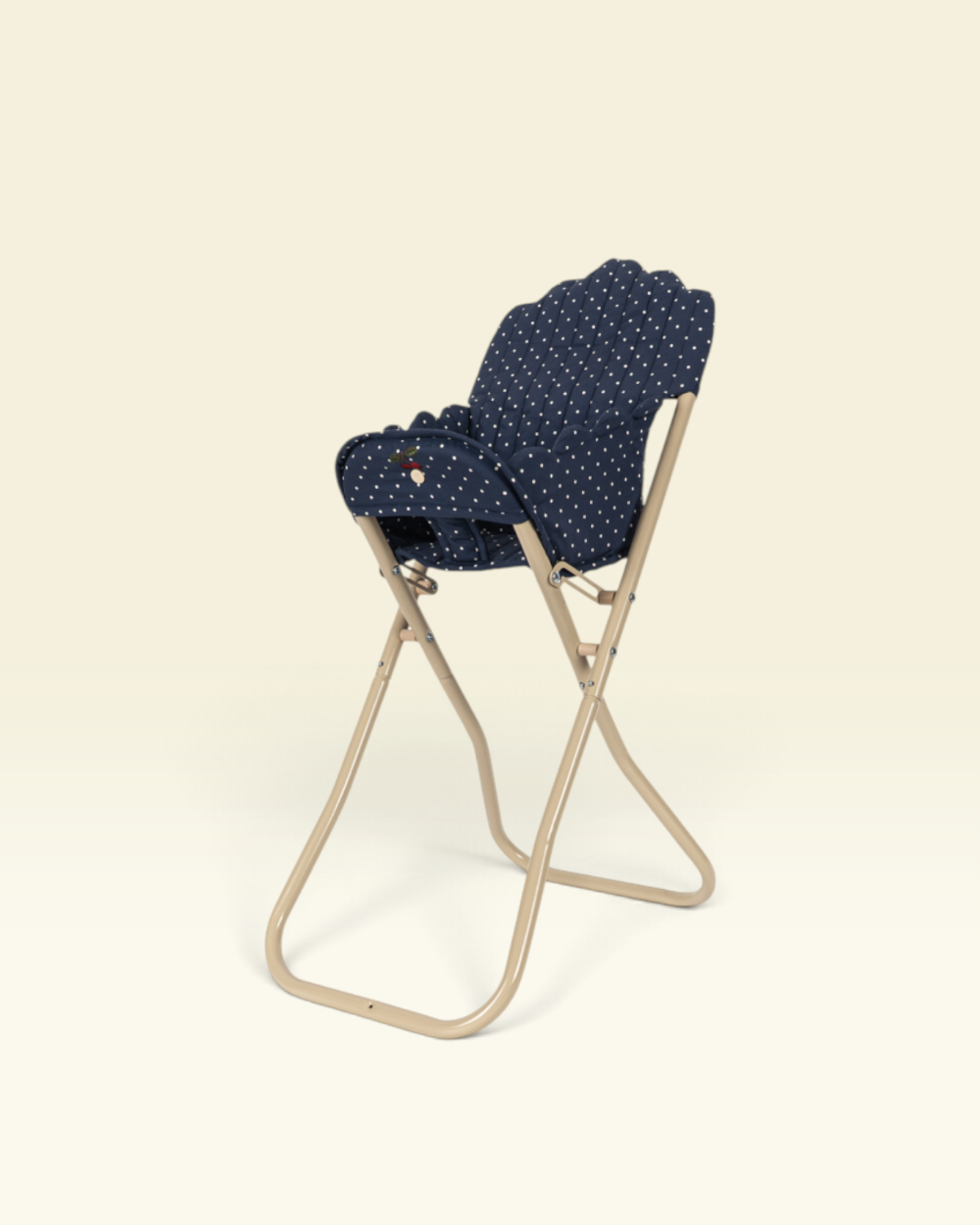 A folding chair with a beige metal frame and a navy blue fabric seat cushion featuring a small white polka dot pattern, shown against a solid cream background.