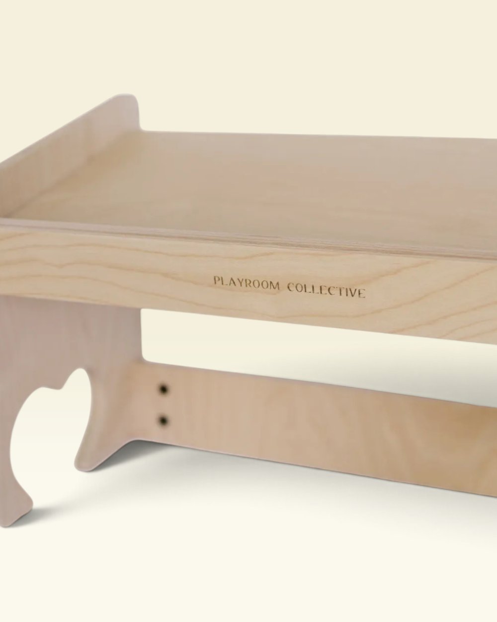 Close-up of a light natural wood playroom organizer or desk shelf with the brand name 'PLAYROOM COLLECTIVE' printed on the side, set against a solid cream background.