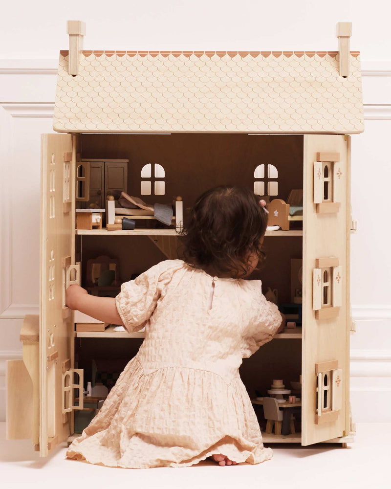 Child playing with a wooden dollhouse on a white floor.