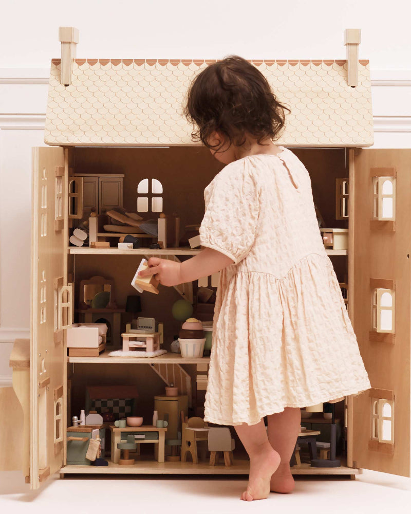 Child playing with a wooden dollhouse in a minimalistic room.