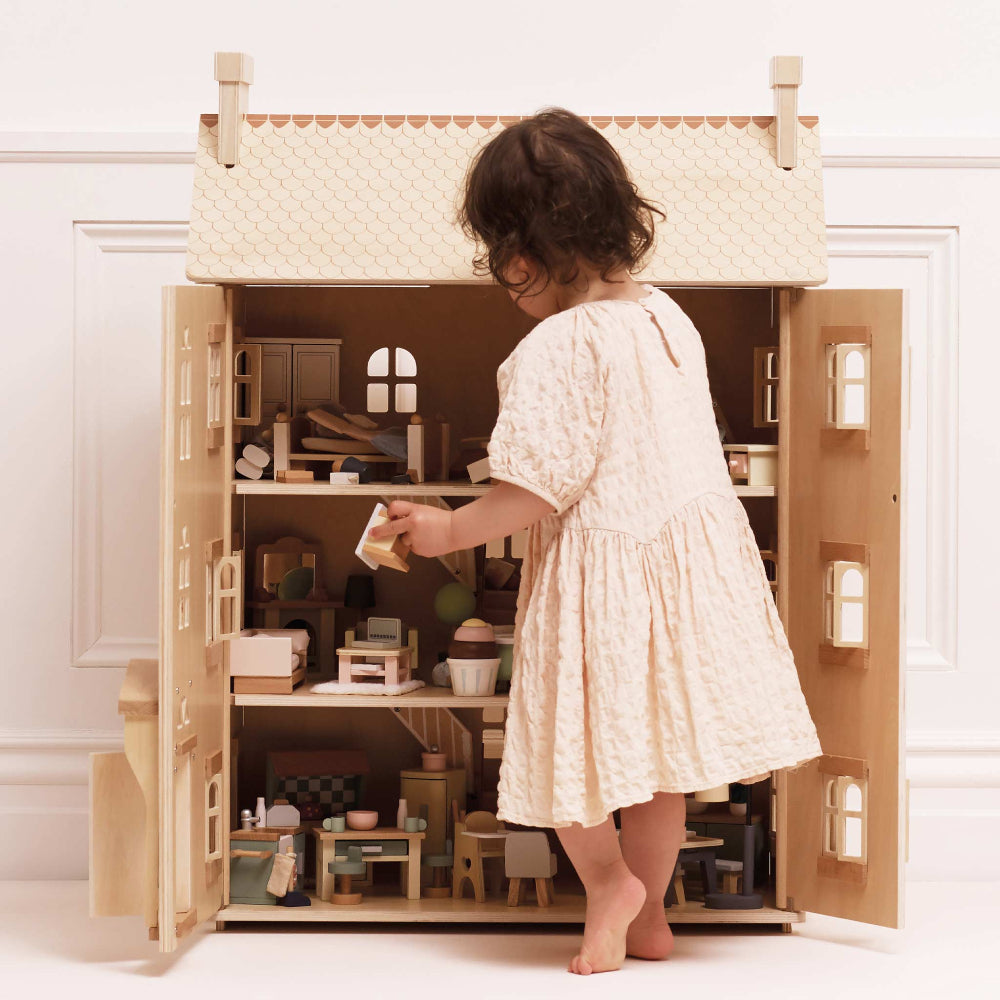 Child playing with a wooden dollhouse in a minimalistic room.