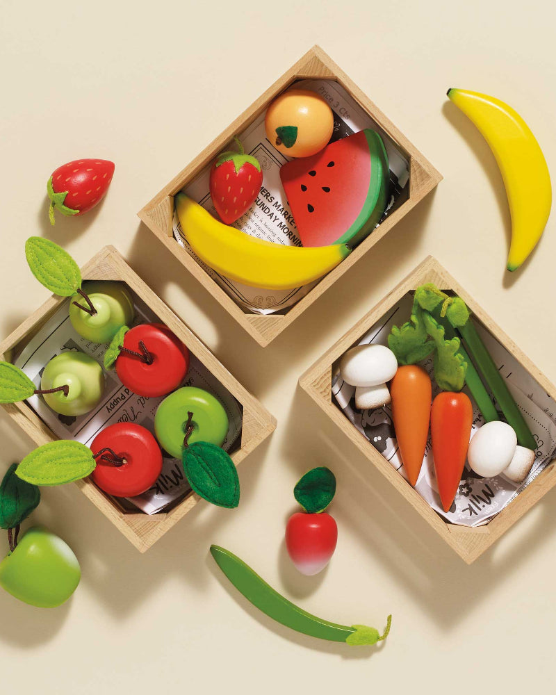Set of toy fruits and vegetables in wooden boxes on a beige background