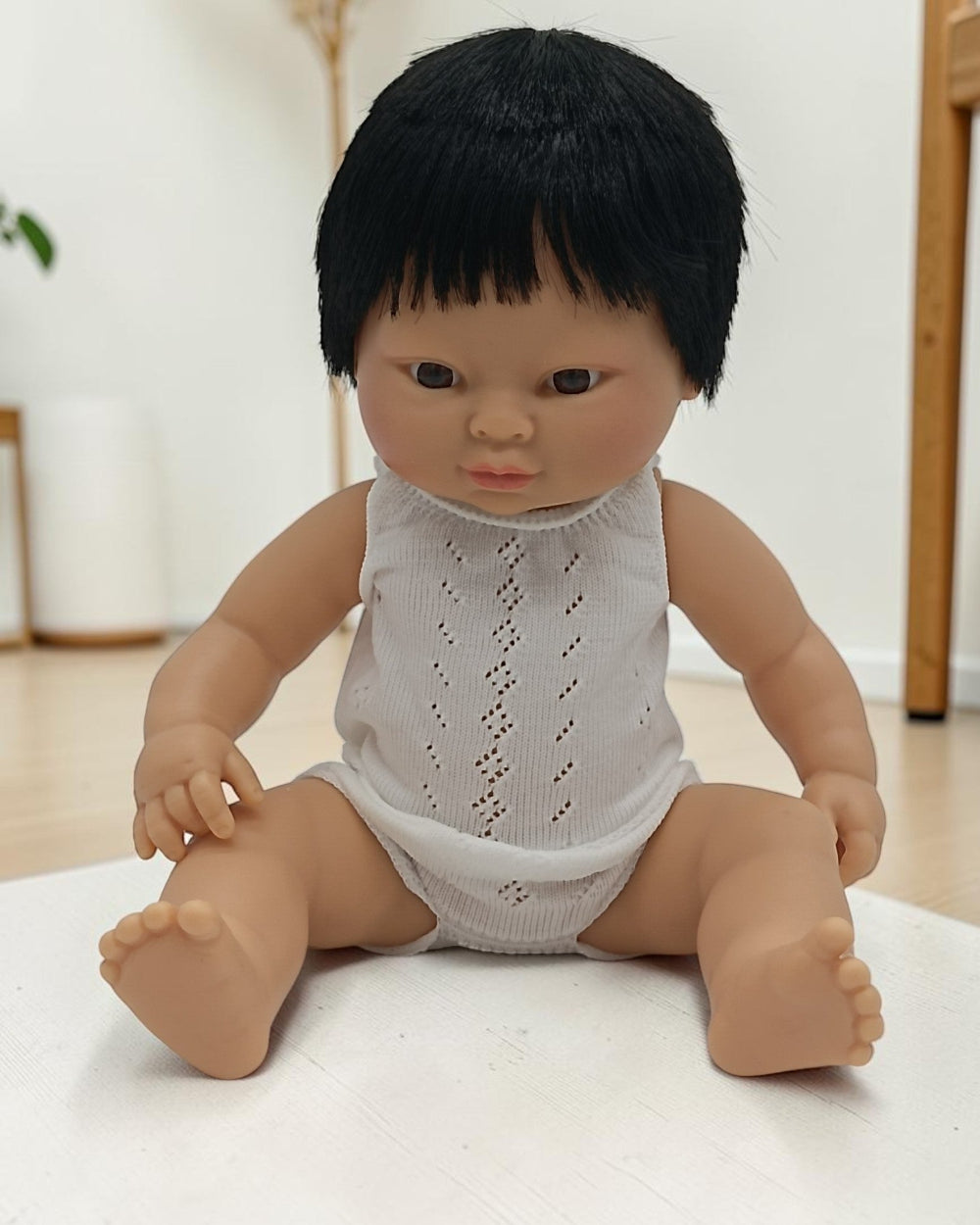 Baby doll with black hair wearing a white lace romper on a light background