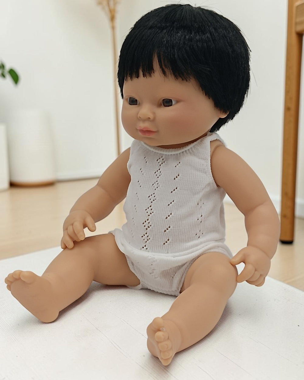 Doll with black hair wearing a white sleeveless top and diaper on a light surface.