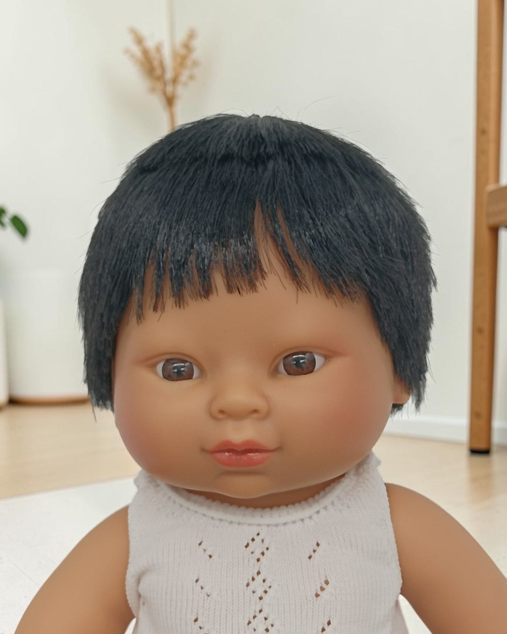Doll with black hair and a white outfit against a neutral background