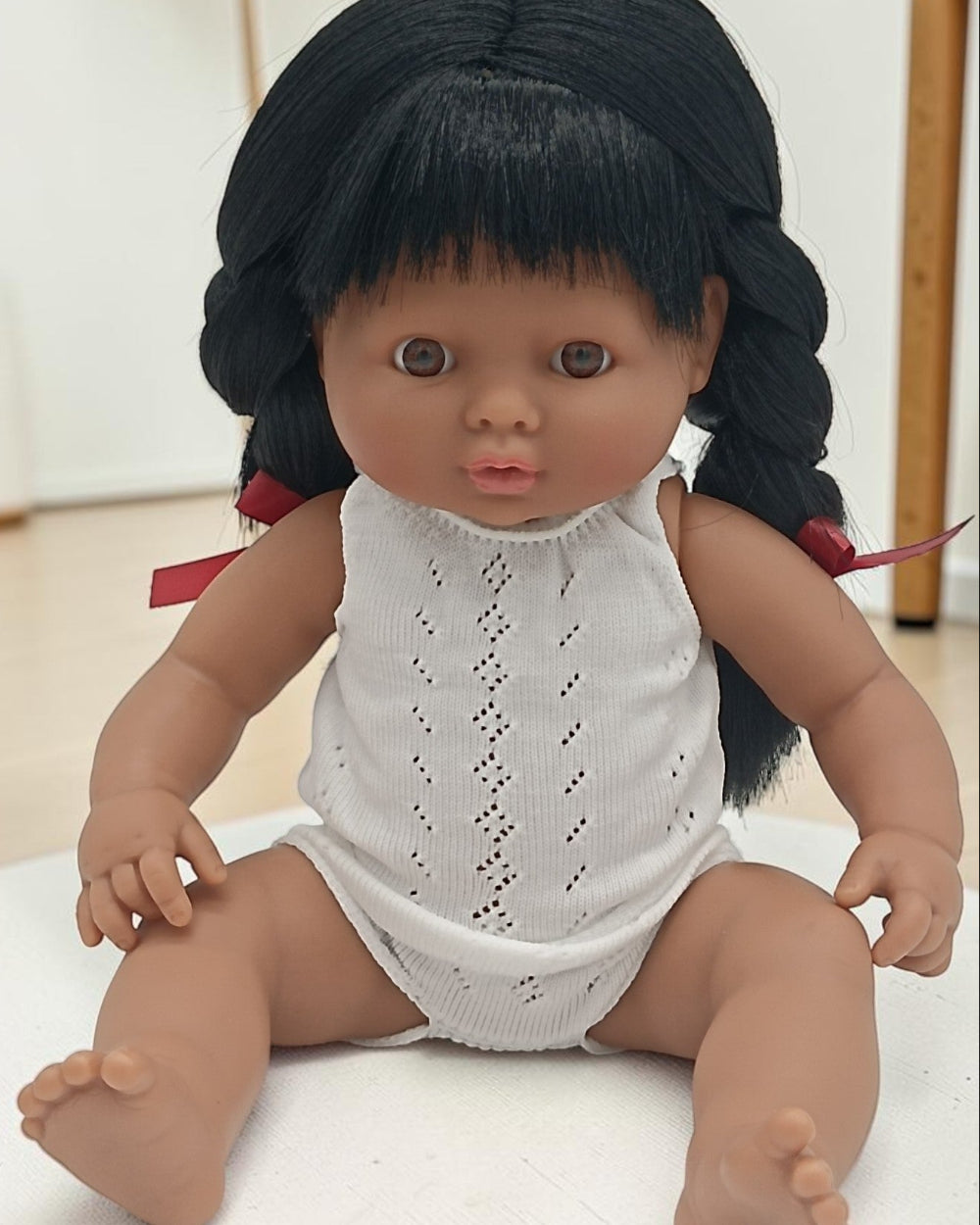 Doll with black hair in pigtails wearing a white outfit on a light background