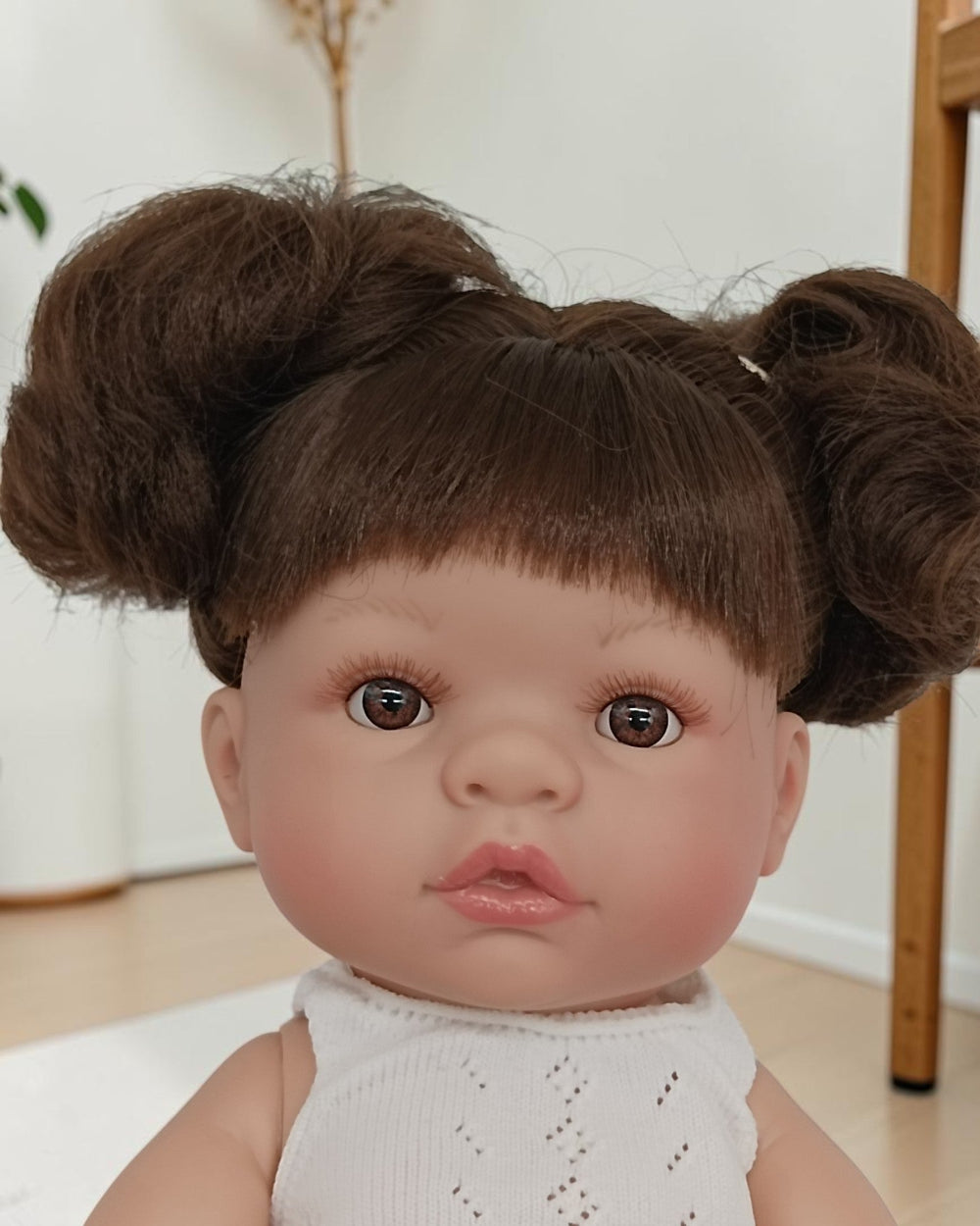 Baby doll with brown hair styled in buns wearing a white outfit.