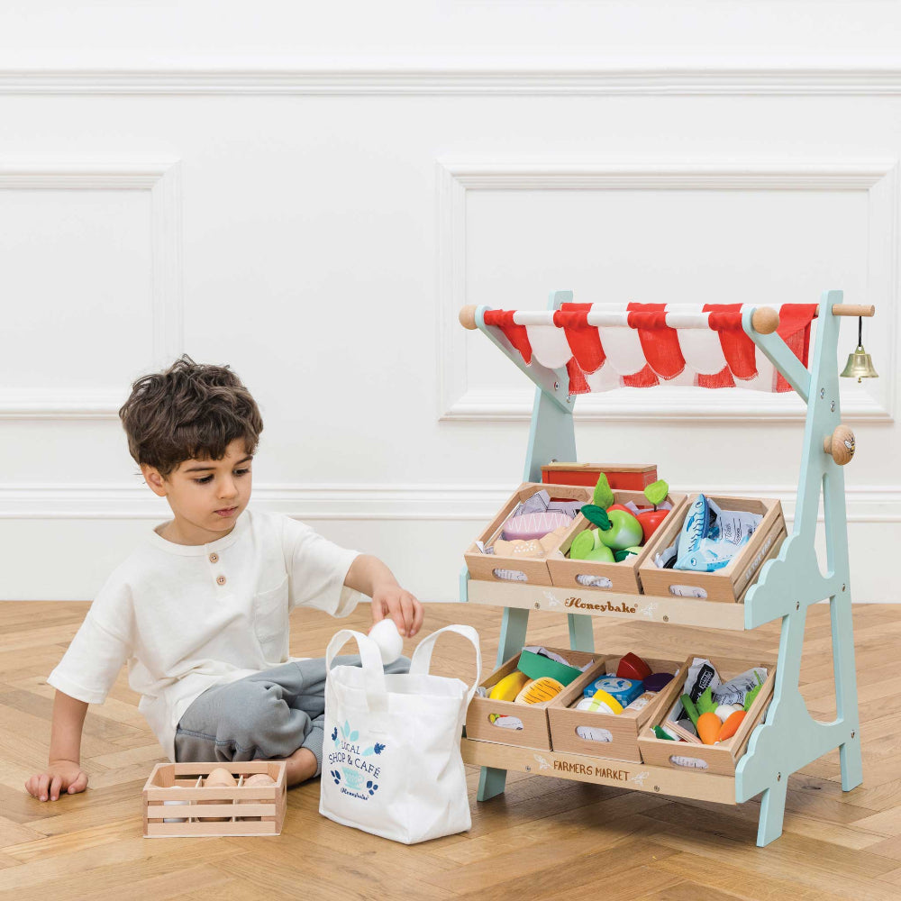 Child playing with a toy farmer's market set on a wooden floor.