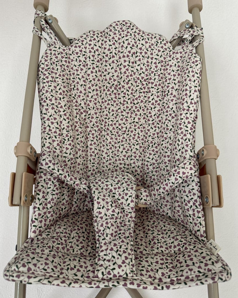 A fabric stroller seat liner with a small-scale floral print in muted pink, green, and purple on an off-white background, shown fitted over a stroller frame.