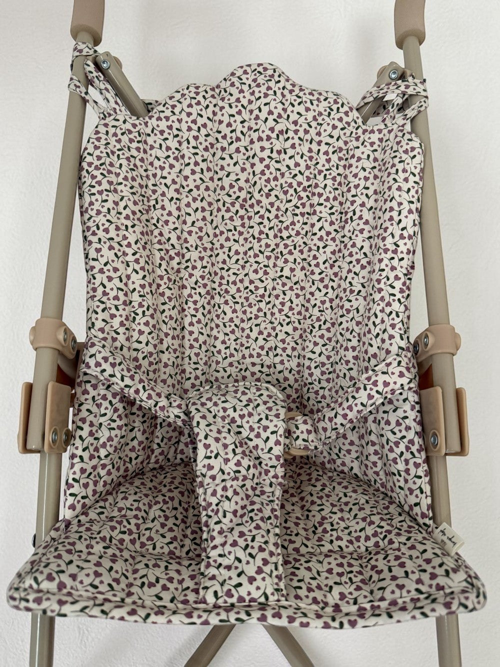 A fabric stroller seat liner with a small-scale floral print in muted pink, green, and purple on an off-white background, shown fitted over a stroller frame.